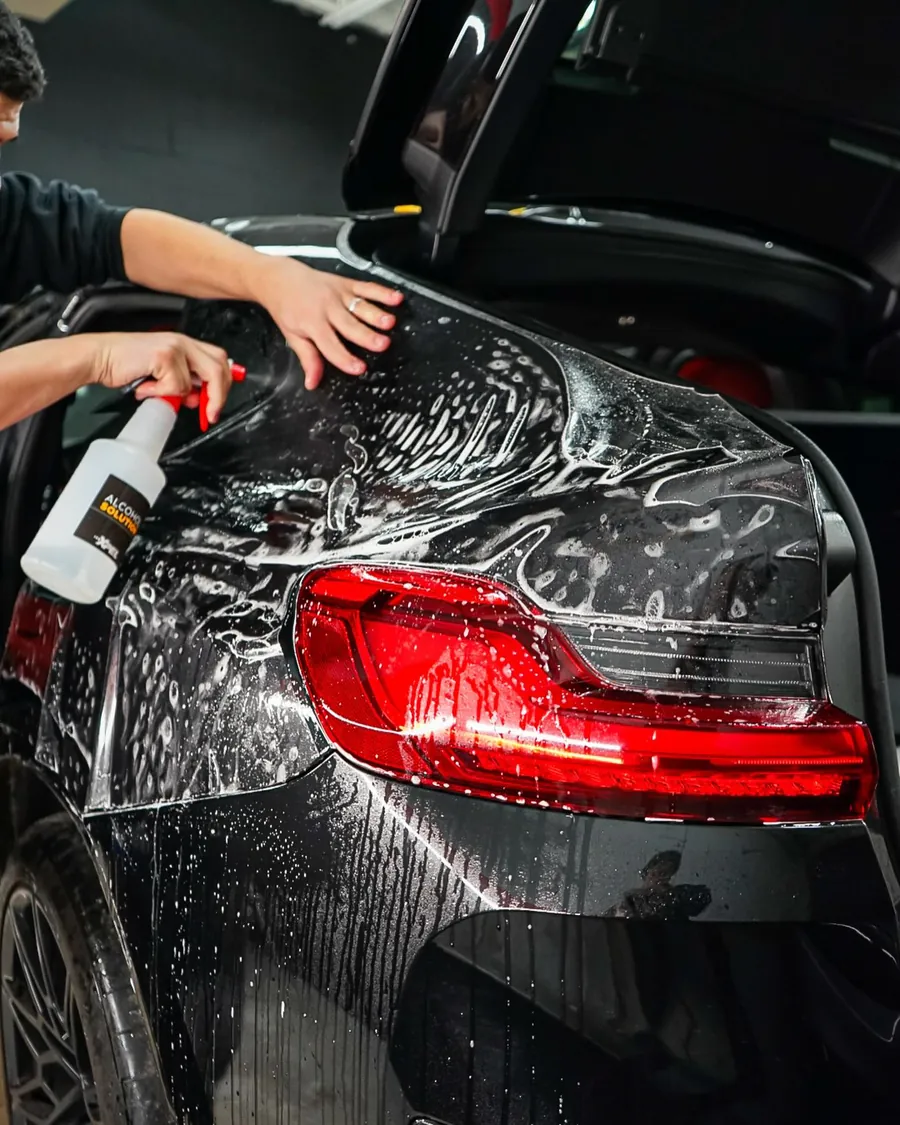 Deux installateurs posent une pellicule de protection humide sur l’arrière d’une BMW, vaporisateur à la main