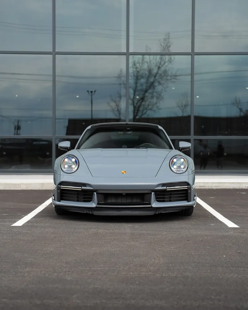 Porsche 911 Turbo S grise vue de face devant un immeuble vitré
